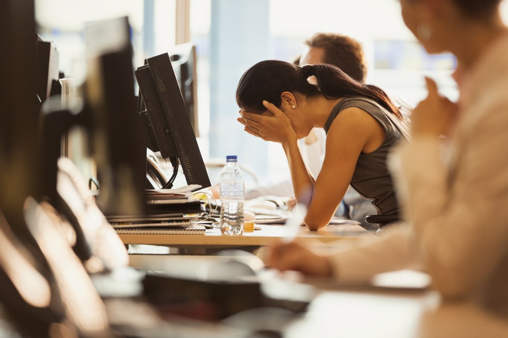 Image: Stressed woman sits with her head in her hands at an office desk