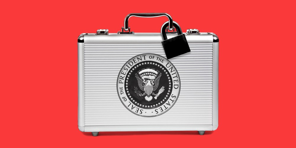 Image: A silver suitcase with a black lock and the seal of the President of the United States sits against a red background