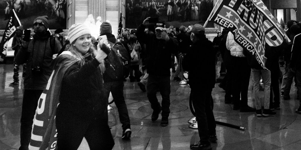 Image: Jenny Cudd wearing a cape that reads, "Trump" takes a photo with her phone amidst other rioters at the US Capitol's Rotunda.