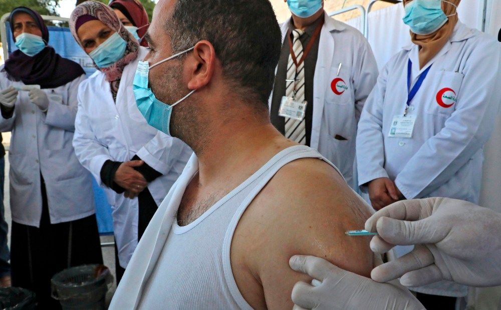 Image: A Palestinian health worker gets vaccinated against COVID-19.