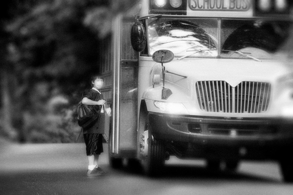 Image: School bus picking up elementary student wearing surgical mask.