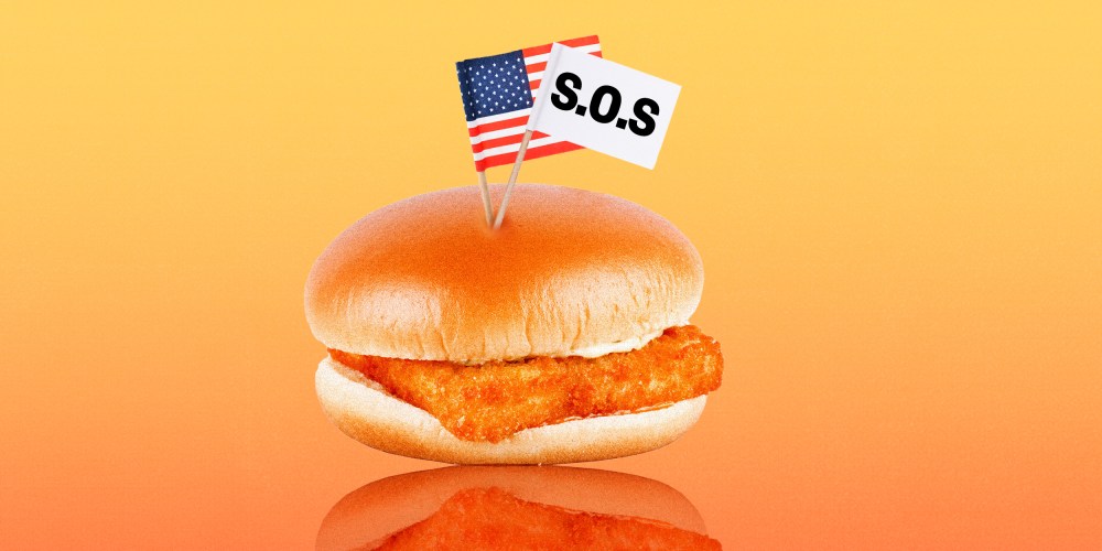 Photo illustration: A fish burger with two small paper flags, one is an American flag and the other is a white flag that reads,"S.O.S."