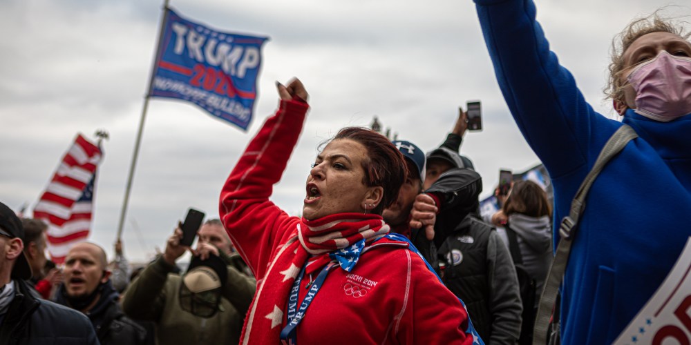 Image: A woman shouting amidst protesters waving the American flag and a flag that reads," Trump 2020".