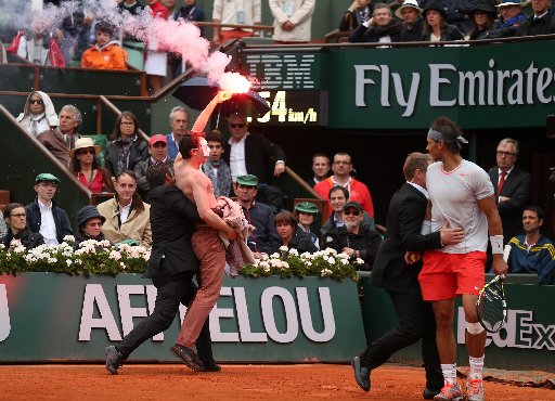 Rafael Nadal of Spain looks on as security guards restrain a protester after he lit a flare and ran on court before the start of a game in the Men's Singles final match between Rafael Nadal of Spain and David Ferrer of Spain on June 9, 2013 in...