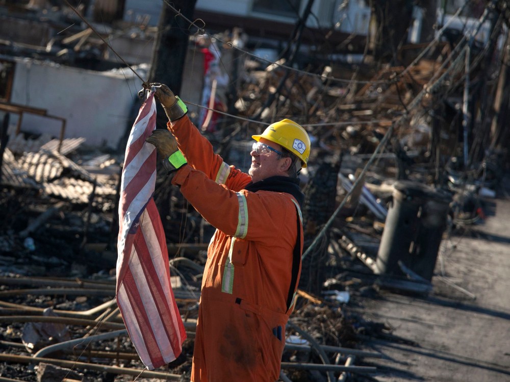 An electrician with Hydro Quebec pulls down a U.S. flag hanging on a cable before testing power lines in Breezy Point neighborhood of Queens. In the worst-hit areas, homes are still without light or heat. (Photo by Adrees Latif/Reuters)