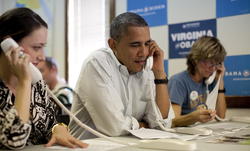President Barack Obama makes phone calls to volunteers at an Organizing for America field office with Alexa Kissinger, left, and, Suzanne Stern, right, Sunday, Oct. 14, 2012, in Williamsburg, Va.