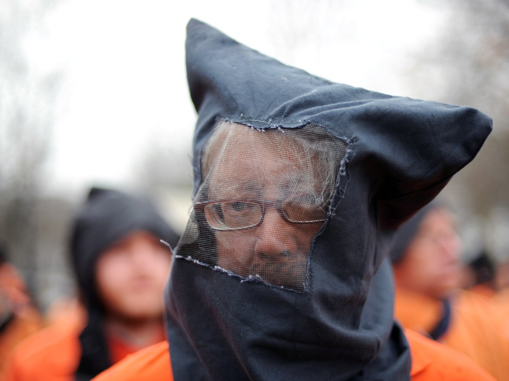File Photo: David Barrows and fellow members of the organization Witness Against Torture wear orange prison jump suits with handcuffs and a hood over their heads during a demonstration urging the government to close down the detention facility at...