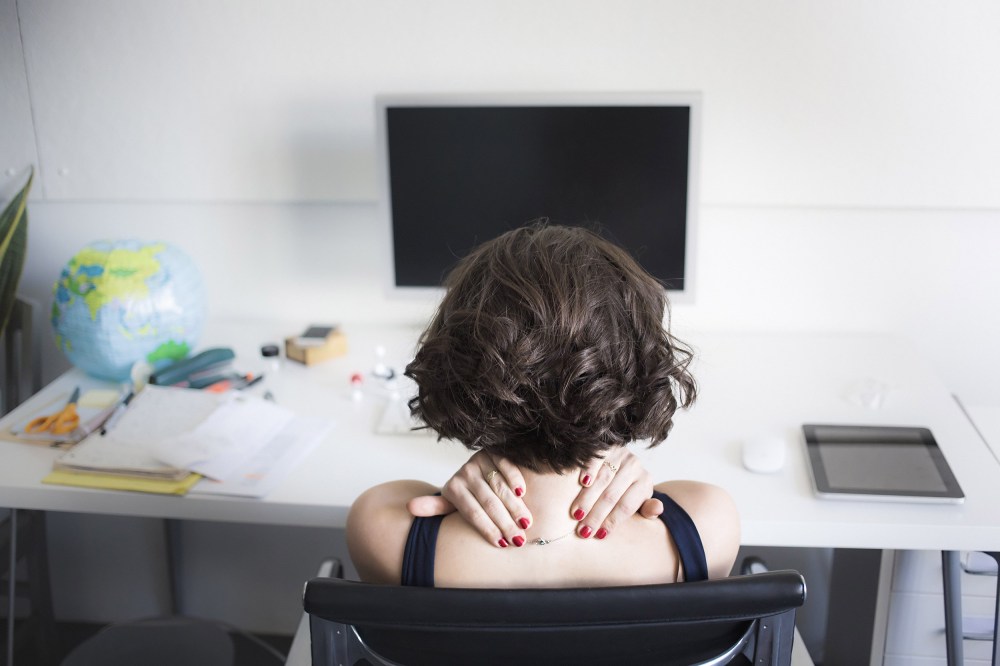 Image: Young woman massaging her neck at desk