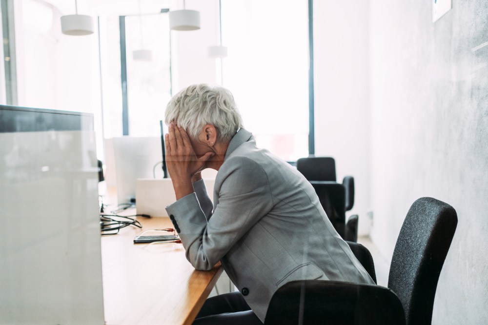 A woman holds her head in her hands at a desk.