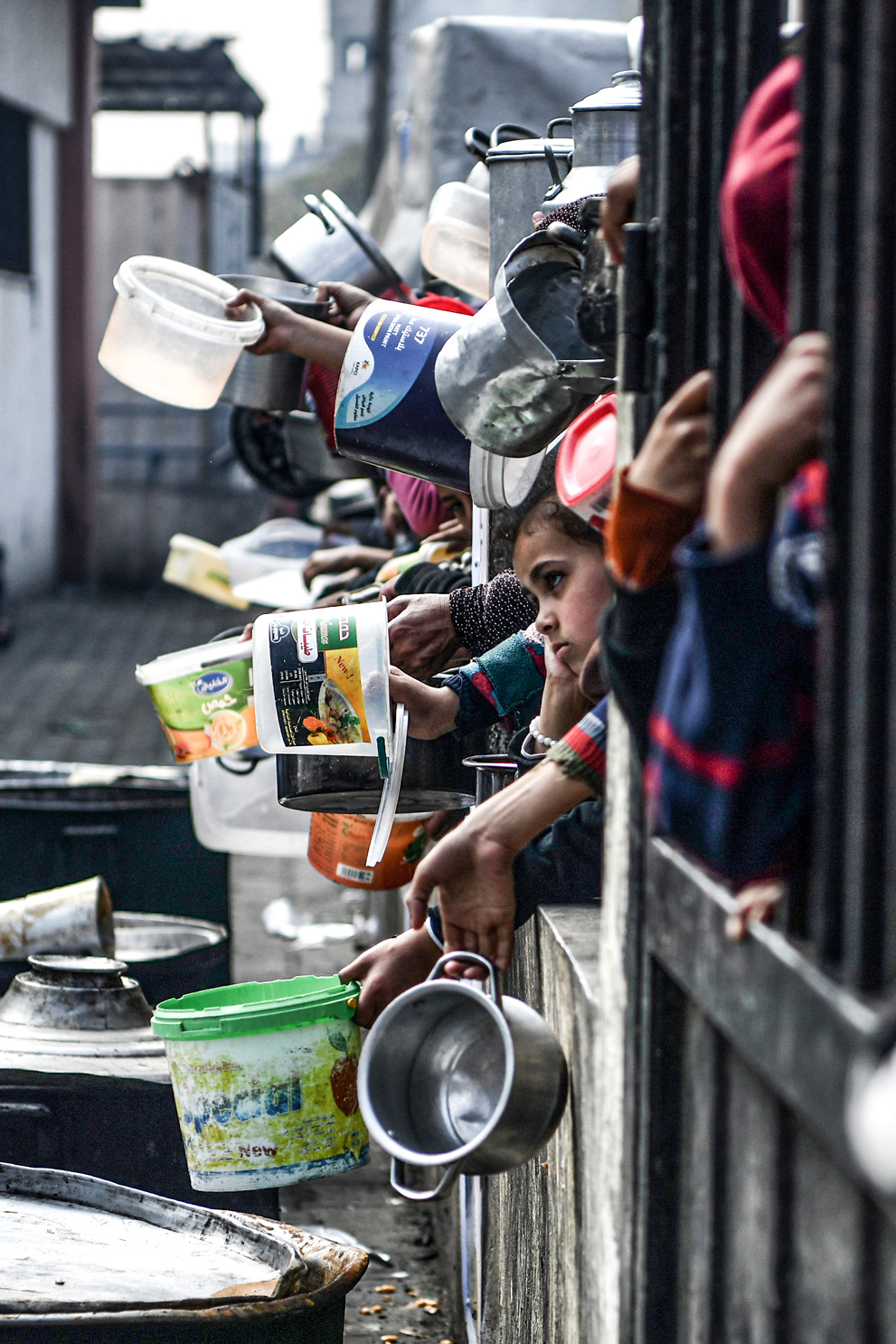 Palestinians hold out their empty containers to be filled with food behind bars.
