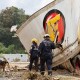 People look through debris near a damaged truck outside with a dog