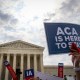 A sign is held up that reads "ACA Is Here To Stay" front of the U.S. Supreme Court.
