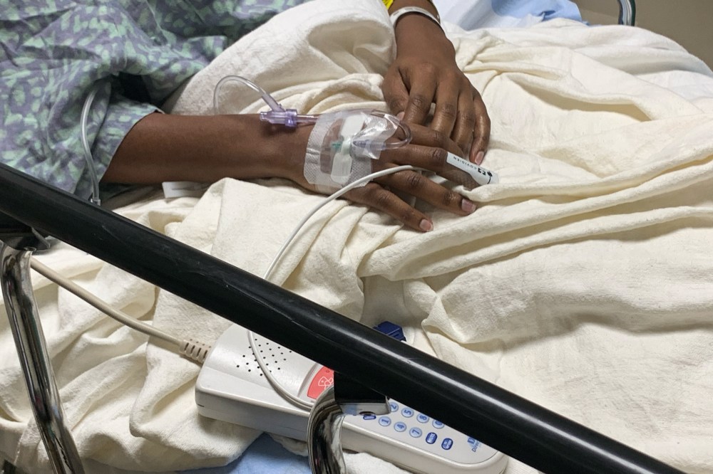 Hands connected to tubes are seen on a hospital bed
