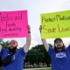 Two people hold signs outside, one the left it says "Medicaid funds critical disability services", and on the right it says "Protect Medicaid, Save lives"