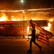 A protester carries a U.S. flag upside down as he walks past a burning building