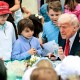 President Donald Trump shows a group of children a trading card of himself while sitting outside