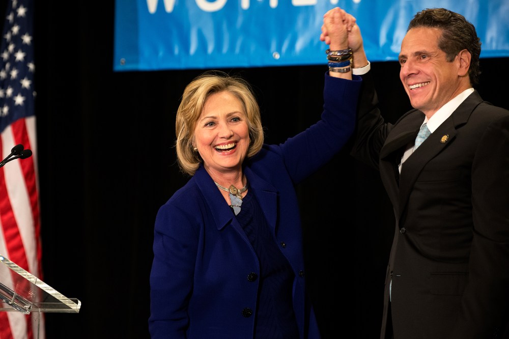 Former U.S. Secretary of State and U.S. Sen. Hillary Rodham Clinton (left) raises the hand of incumbent New York Governor Andrew Cuomo (right) laugh during a "Women for Cuomo" campaign event on Oct. 23, 2014 in New York, NY. (Photo by Bryan Thomas/Getty)