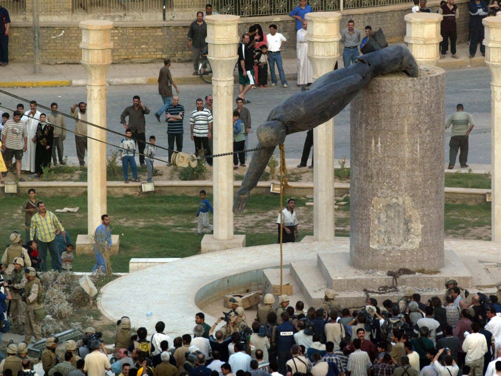 Iraqis watching a statue of Iraqi President Saddam Hussein as it is pulled down in Baghdad's al-Fardous square on April 9, 2003. (Photo by Patrick Baz/AFP/Getty Images, File)