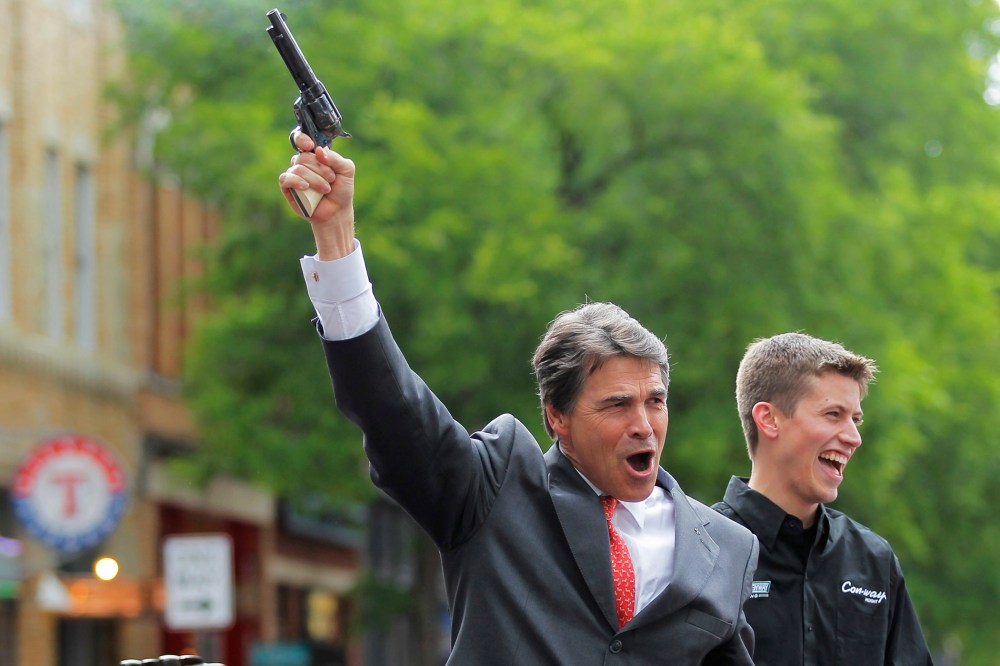 Texas Republican Gov. Rick Perry fires a six shooter filled with blanks as NASCAR driver Colin Braun looks on at an event in downtown Fort Worth, Texas on April 15, 2010.
