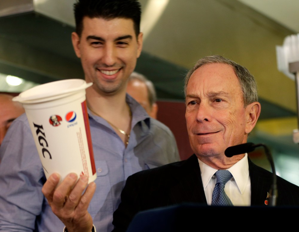 New York City Mayor Michael Bloomberg looks at a 64oz cup, as Lucky's Cafe owner Greg Anagnostopoulos, left, stands behind him, during a news conference at the cafe in New York, Tuesday, March 12, 2013. (AP Photo/Seth Wenig)