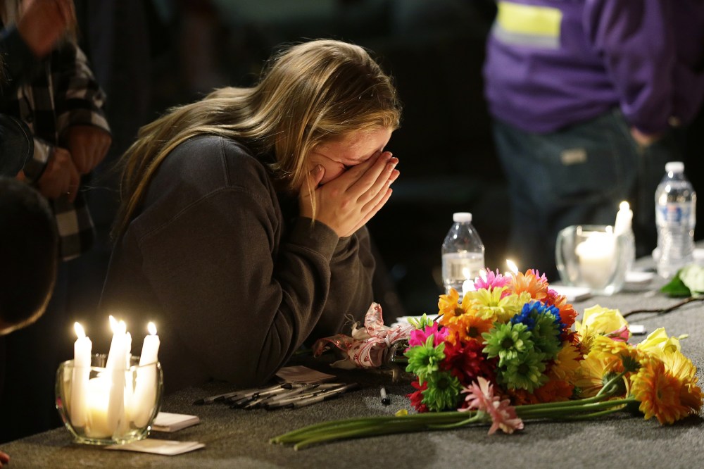 A young woman holds her head in her hands as she kneels before candles and flowers placed on the stage at the Grove Church in Marysville, Wash., Oct. 24, 2014, after a memorial vigil held for people affected by a shooting at Marysville Pilchuck High Schoo