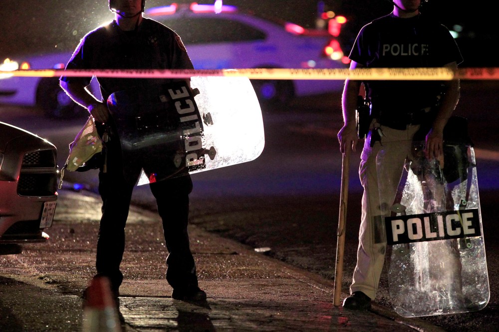 Police wearing riot gear stand at a post as they wait for a crowd to disperse, Aug. 11, 2014, in Ferguson, Mo.