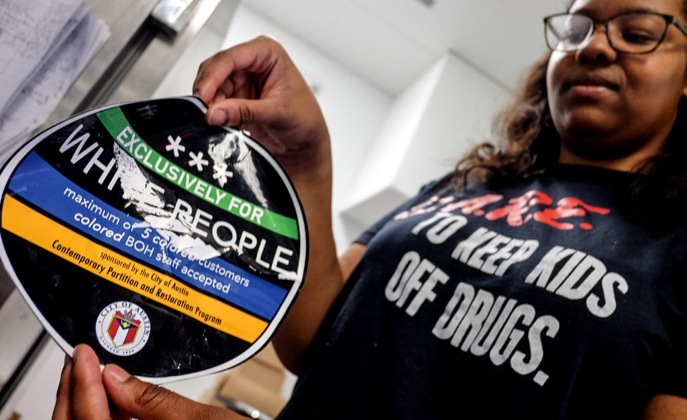 April Jensen, an employee at Sugar Mama's holds a sticker that the business found on the front of their store in Austin, Texas, March 18, 2015. (Photo by Austin American-Statesman, Rodolfo Gonzalez/AP)