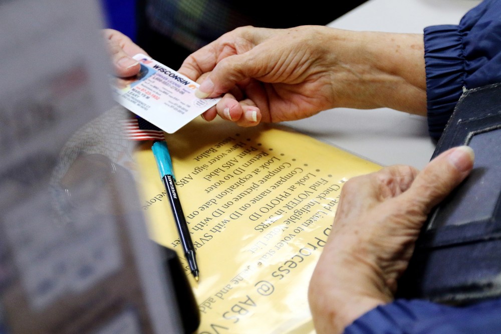 A voter in Eau Claire, Wis. hands her photo identification card to an election assistant on March 21, 2016, at the City of Eau Claire Elections Office. (Photo by Marisa Wojcik/The Eau Claire Leader-Telegram/AP)