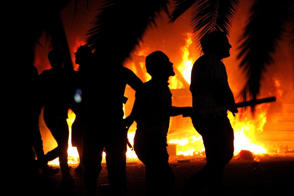 In this Friday, Sept. 21, 2012 file photo, Libyan civilians watch fires at an Ansar al-Shariah Brigades compound, after hundreds of Libyans, Libyan Military, and Police raided the Brigades base, in Benghazi, Libya. (Photo by Mohammad Hannon/AP)