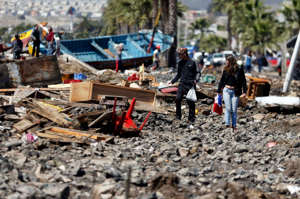 People walk through debris left behind by an earthquake-triggered tsunami in the coastal town of Coquimbo, Chile on Sept. 17, 2015. (Photo by Luis Hidalgo/AP)