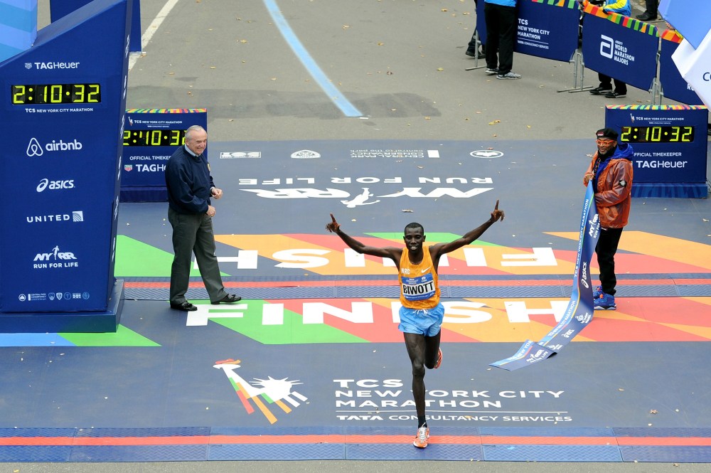 Stanley Biwott of Kenya crosses the finish line to win the Pro Men's division in the NYC Marathon. Police Commissioner William J. Bratton and marathon Grand Marshal Spike Lee hold up the finish ribbon, Nov. 1, 2015. (Photo by Craig Barritt/Getty)