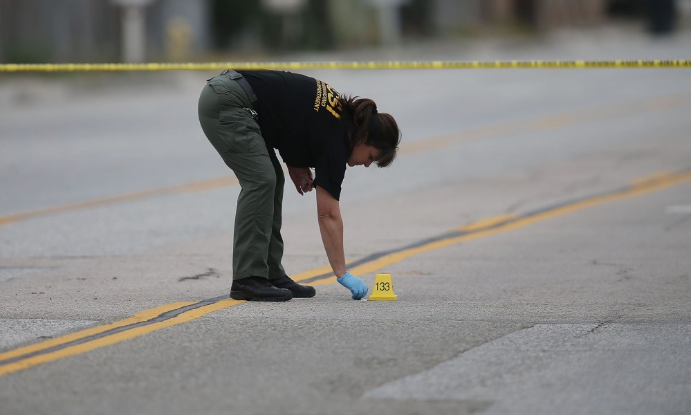 A Law enforcement officer picks up as shell casing near the Ford SUV vehicle that was the scene where suspects of the shooting at the Inland Regional Center were killed on Dec. 4, 2015 in San Bernardino, Calif. (Photo by Joe Raedle/Getty)
