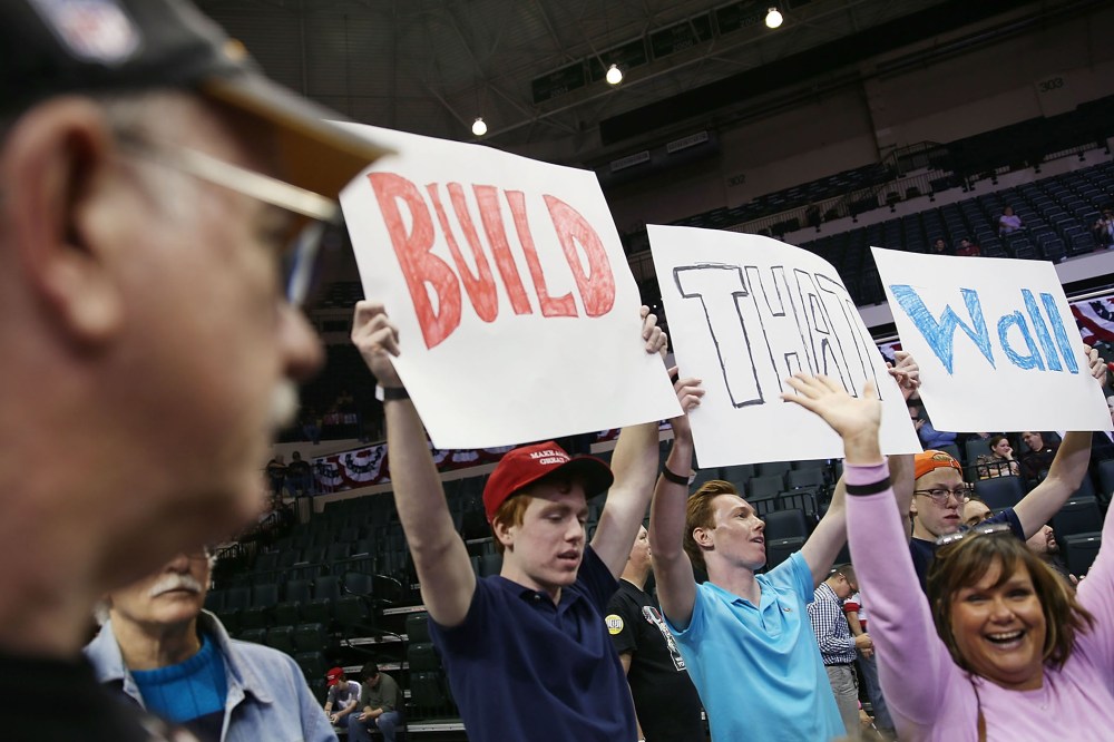 People hold signs that read, " Build that Wall", as they wait for the start of a campaign rally for Republican presidential candidate Donald Trump at the University of South Florida on Feb. 12, 2016 in Tampa, Fla. (Photo by Joe Raedle/Getty)