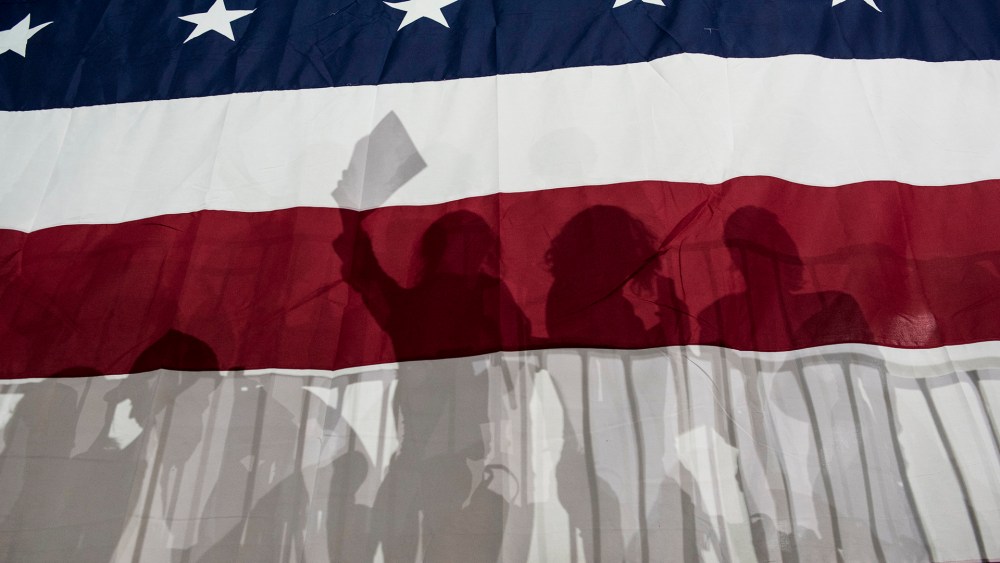 Political supporters are silhouetted in a large American flag on March 2, 2016. (Photo by Andrew Renneisen/Getty)