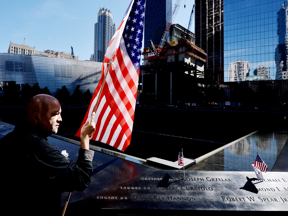 NEW YORK - SEPTEMBER 11: Marshall Rodriguez of New York holds an American flag at the edge of the South Pool while visiting the names of friends he lost during memorial ceremonies for the eleventh anniversary of the terrorist attacks on lower...