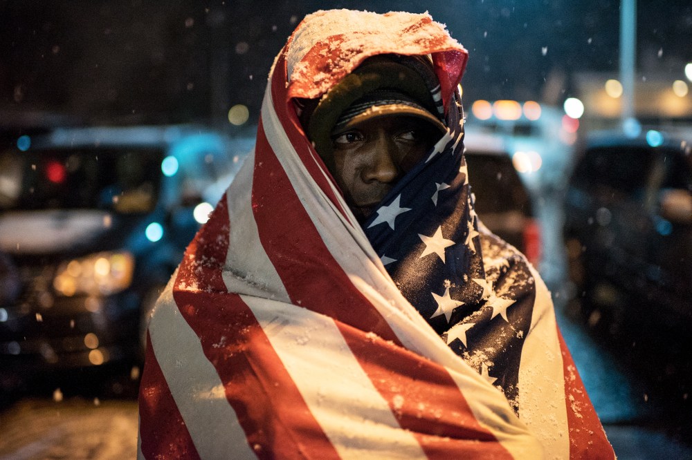 A protester covered in a U.S. flag stands in front of Ferguson Police Department as the snow falls, in Ferguson, Mo. on Nov. 26, 2014. (Photo by Alexey Furman/EPA)
