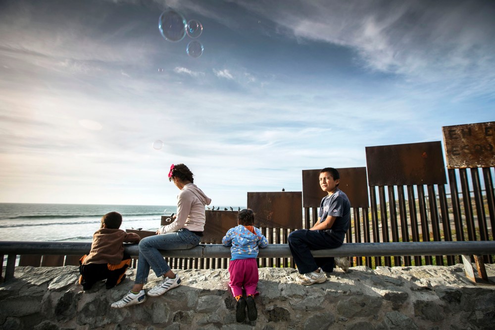 Children sit alongside the border fence beside the sea that divides Mexico from the United States, in Tijuana, Mexico.