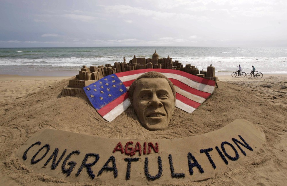 Cyclists ride on a beach passing by a sand sculpture congratulating U.S. president Barack Obama for a second term in office in Puri, India.(AP Photo/Biswaranjan Rout)