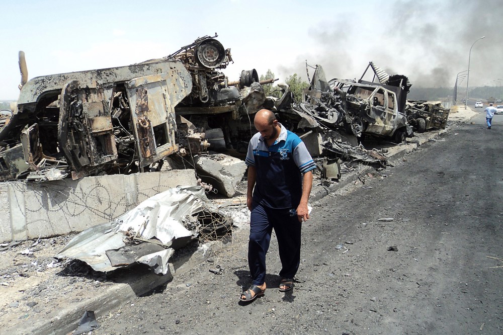 A man walks past near remains of burnt vehicles belonging to Iraqi security forces in the northern Iraq city of Mosul on June 13, 2014.
