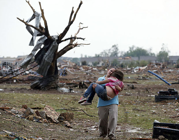 A woman carries a child through a field near the collapsed Plaza Towers Elementary School in Moore, Okla., Monday, May 20, 2013. A tornado as much as a mile wide with winds up to 200 mph roared through the Oklahoma City suburbs Monday, flattening...