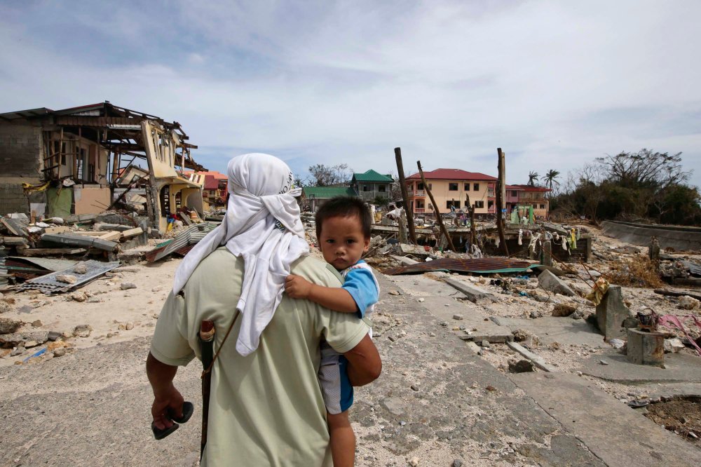 A man walks home with his son Monday Nov. 11, 2013, following Friday's devastating typhoon that lashed Hernani township, in eastern Samar province, in the central Philippines.