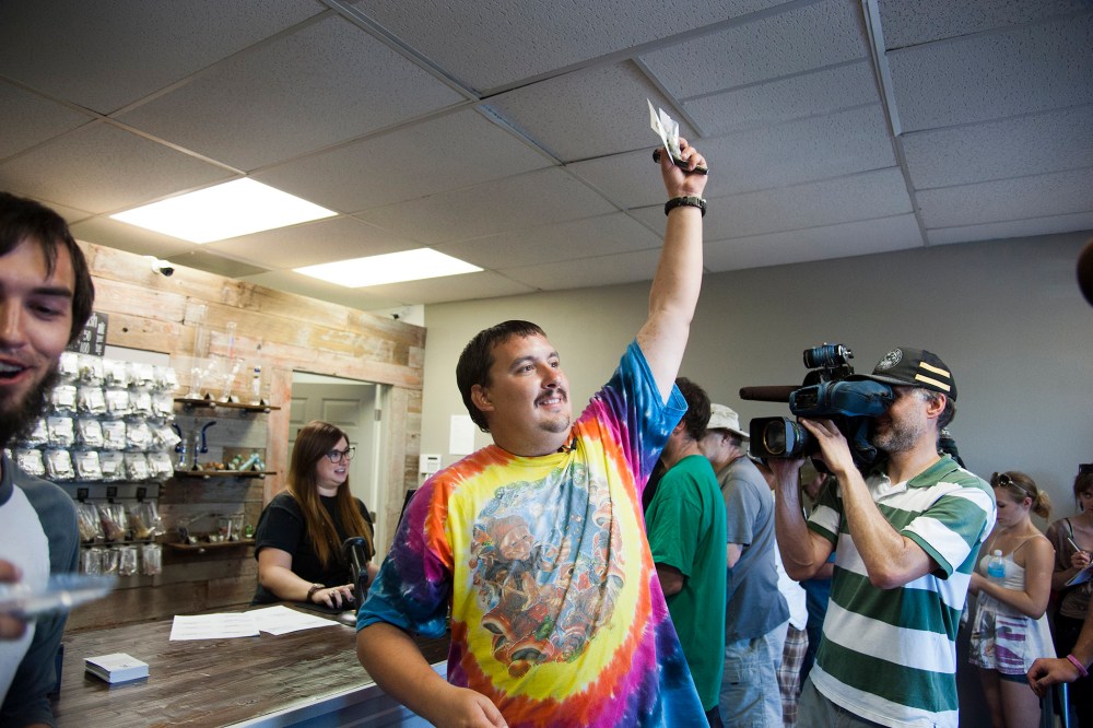Mike Boyer turns to the crowd outside, showing off the 4 grams of marijuana he bought as the first in line to legally purchase marijuana in Spokane, Wash, July 8, 2014.