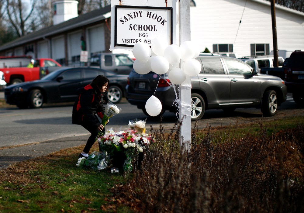 A girl places flowers at a memorial at a sign for Sandy Hook Elementary School in Sandy Hook, Conn.