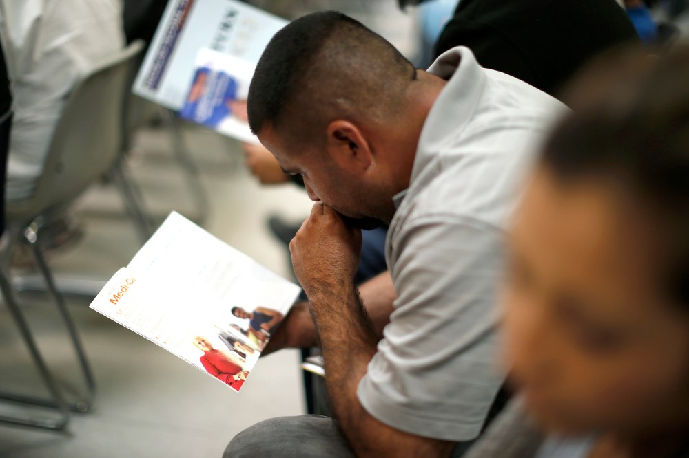 People read pamphlets as they wait in line at a health insurance enrollment event in Cudahy, California on March 27, 2014.