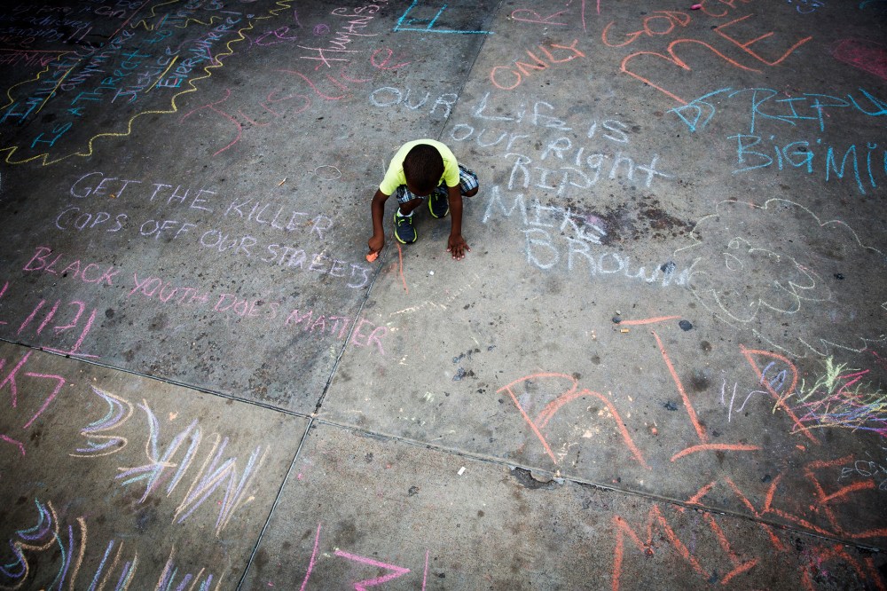 A young boy uses sidewalk chalk to draw on a parking lot filled with memorial slogans during a demonstration to protest the shooting of Michael Brown and the resulting police response to protests, in Ferguson, Mo, Aug. 15, 2014.