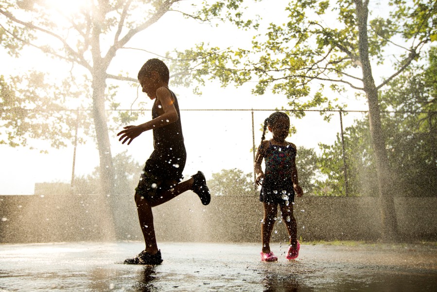 Children run through a sprinkler system installed inside a playground to cool off during a hot summer day in New York
