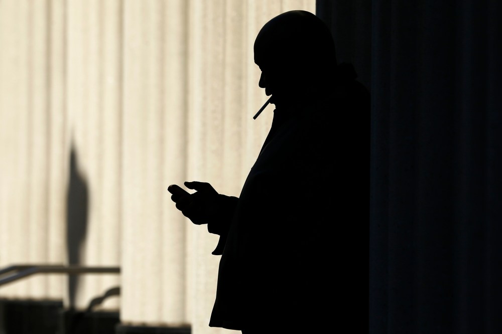 A man on his mobile phone as he smokes a cigarette outside, Dec. 9. 2013, in San Diego, Calif.
