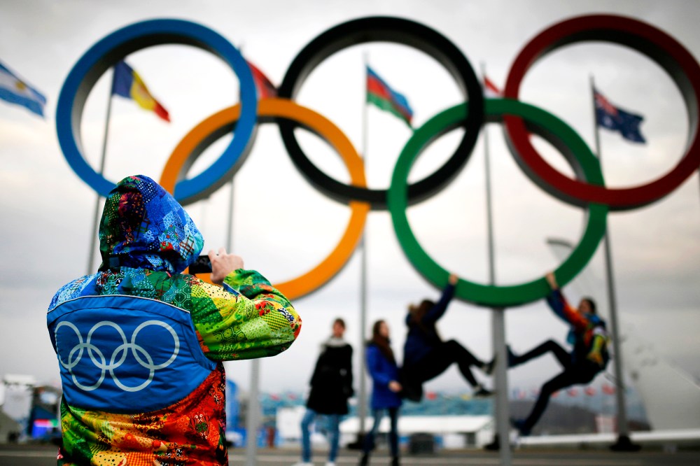 An Olympic volunteer takes pictures of people as they pose under the Olympic rings in Sochi, Jan. 30, 2014.