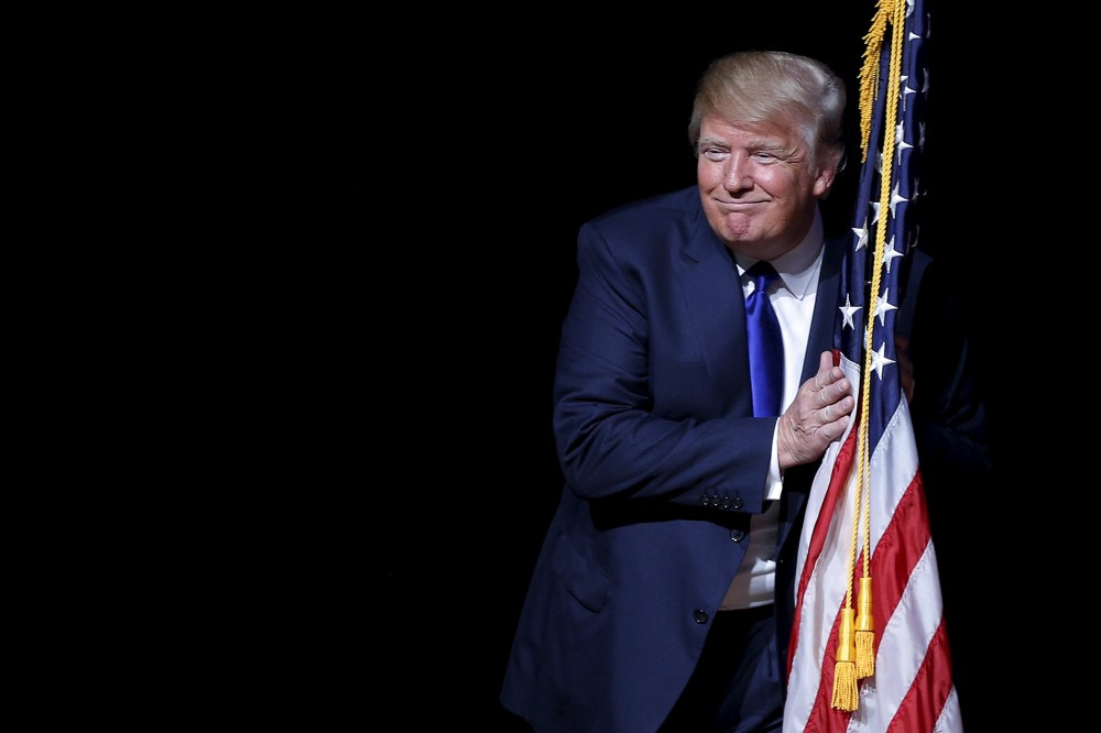U.S. Republican presidential candidate Donald Trump hugs a U.S. flag as he takes the stage for a campaign town hall meeting in Derry, N.H., Aug. 19, 2015. (Photo by Brian Snyder/Reuters)