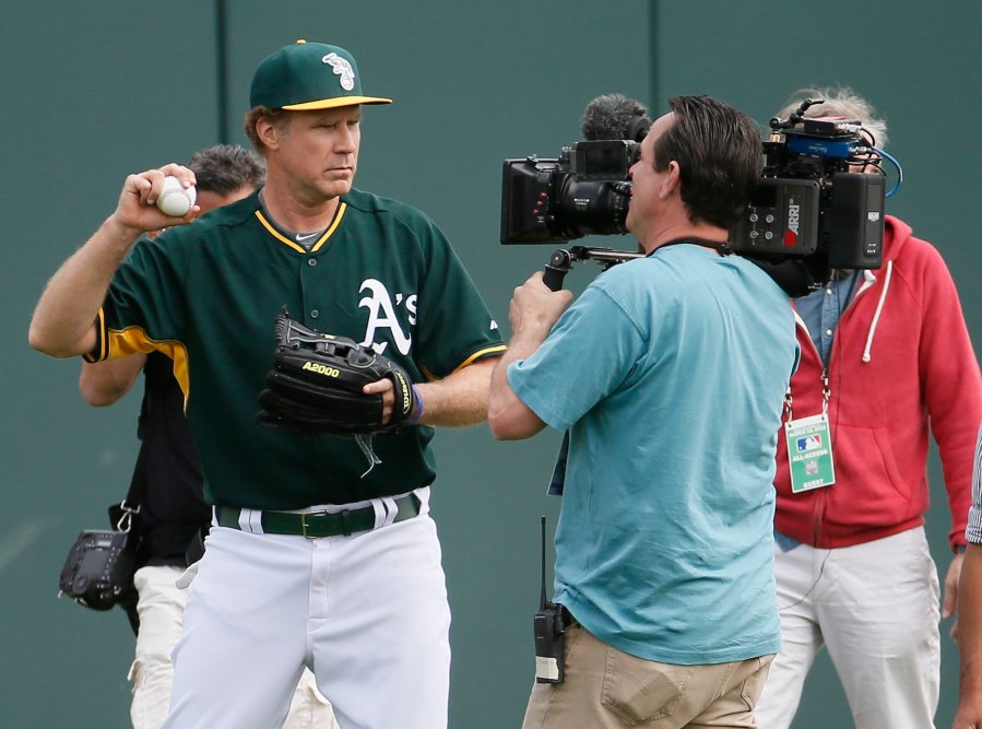 Actor Will Ferrell, left, warms up for the Oakland Athletics prior to the first inning of a spring training baseball game against the Seattle Mariners, on March 12, 2015, in Mesa, Ariz.